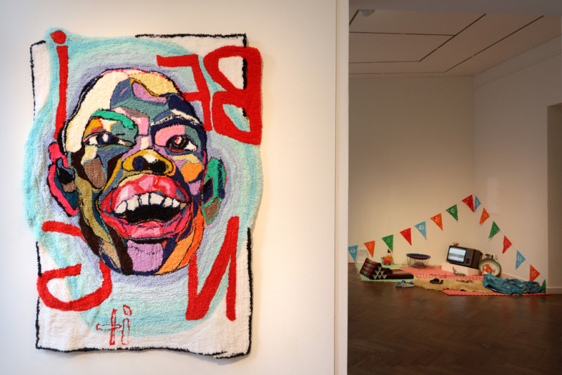 ein Teppich mit einem bunten Gesicht hängt an der Wand