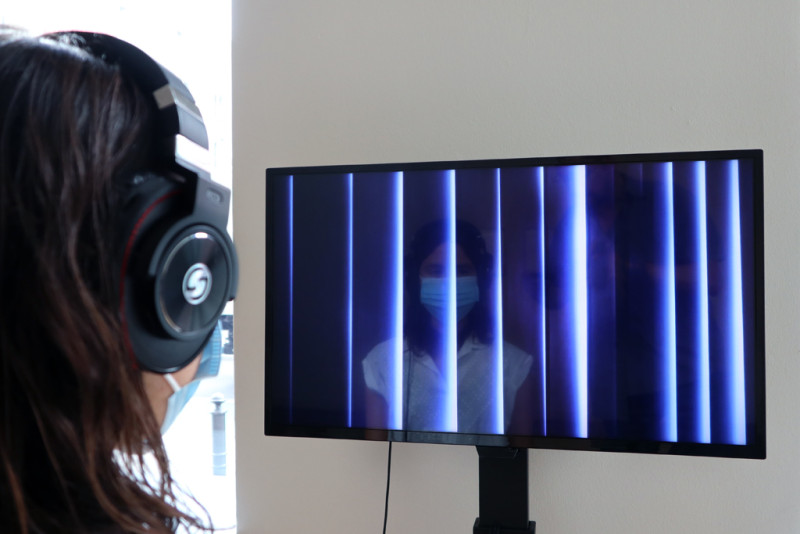 eine Besucherin mit Mundschutz und Kopfhörern sieht sich das Video der Künstlerin an