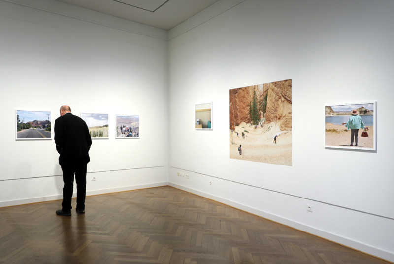 Fünf Fotografien in querformatigen weißen Bilderrahmen und ein Wandposter zeigen Eindrücke der Reise von Franca Wohlt und ihrer Mutter in den Südwesten der USA. Ein Besucher auf der linken Seite betrachtet eine der Fotografien.