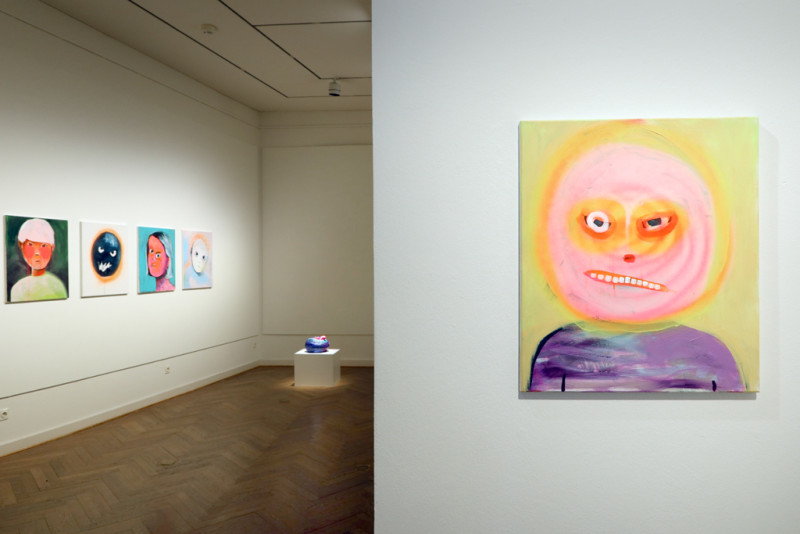 View through the premises. A picture with an angry face in the foreground. There are more pictures hanging in the back.