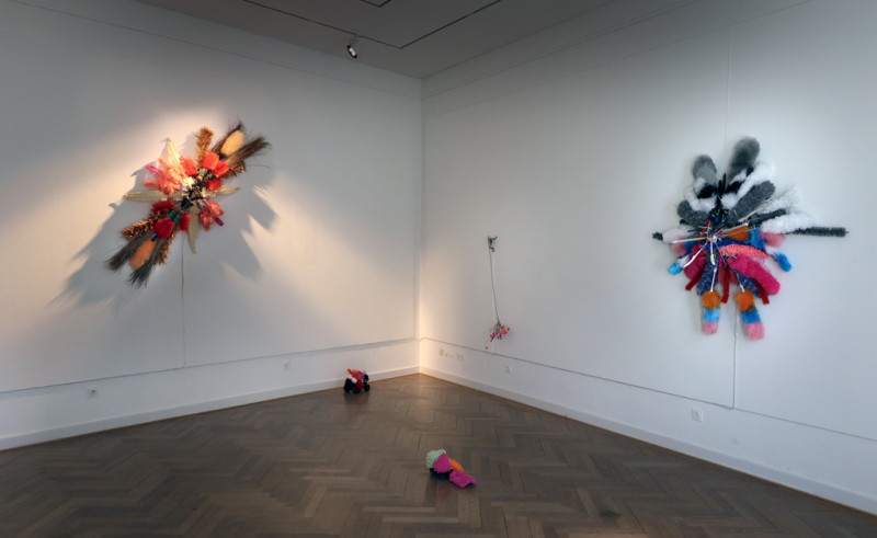 Drei Objekte aus verschiedenen Putzutensilien hängen an der Wand und am Boden liegen zwei kleine Arbeiten aus Putzutensilien, die auf vergesteuerten Autos befestigt sind.