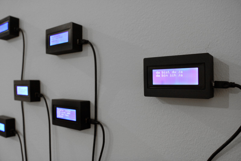 Kleinformatige Displays hängen an der Wand, auf denen fragmentarisch Sätze aufleuchten