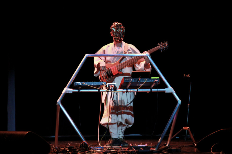 Vor einem silbernen Gestell steht ein Mann mit goldener Maske