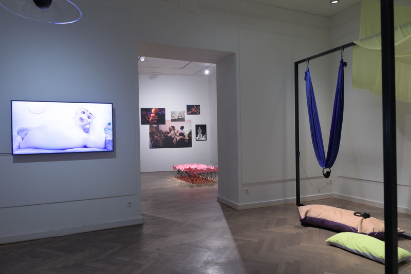 The picture shows a screen with video work and next to it steel frames with colored textiles