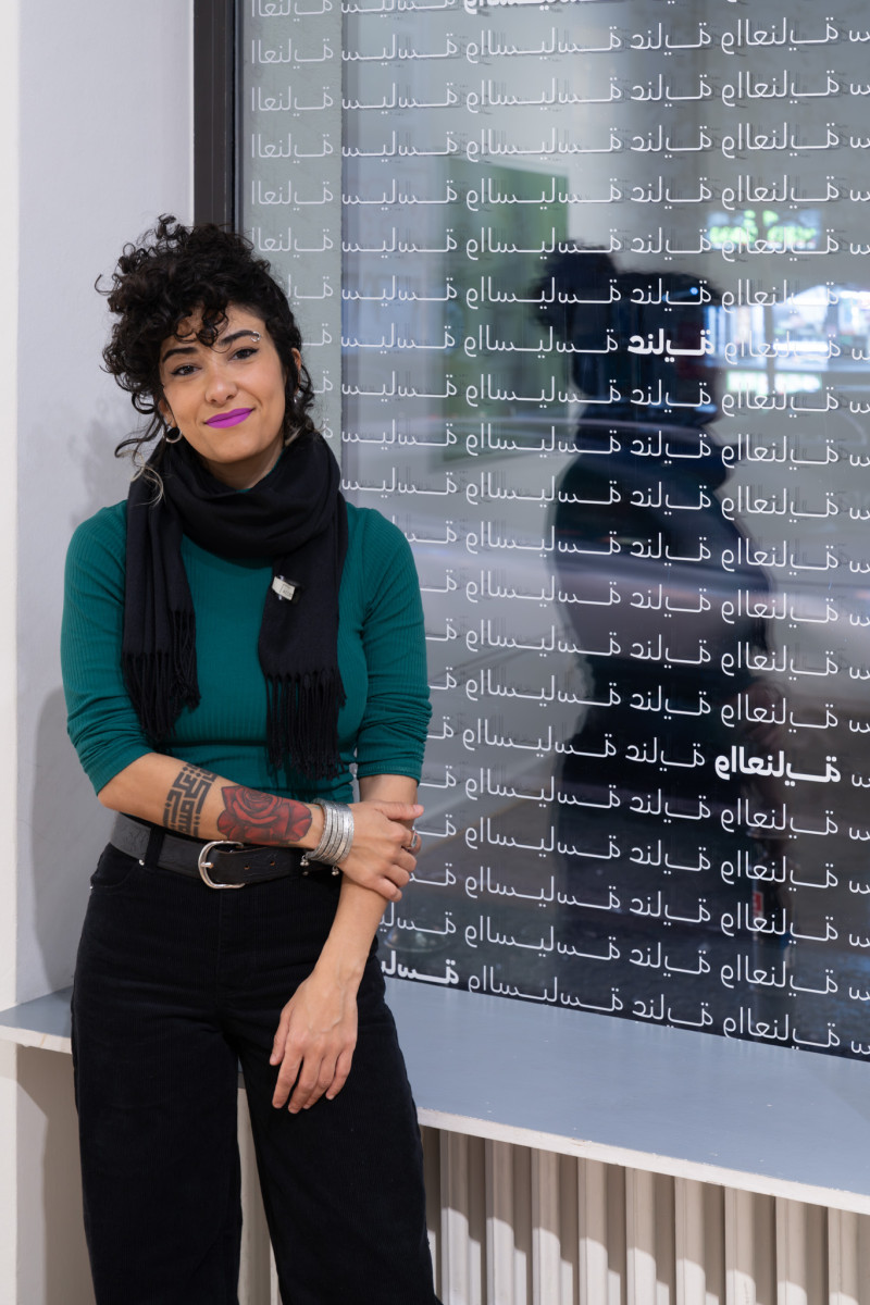 Die Künstlerin steht vor einem Fenster. Darauf ist arabische Schrift angebracht.