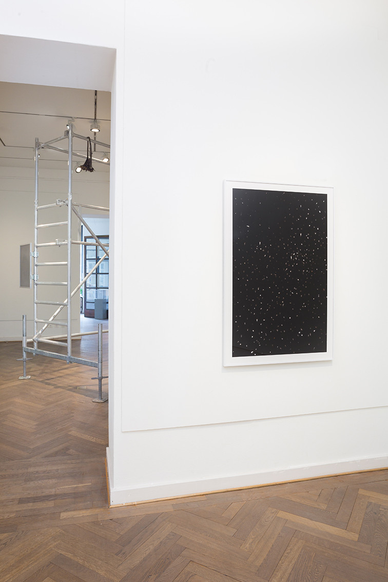 The picture shows scaffolding in the background and a black photo print with white spots in the foreground