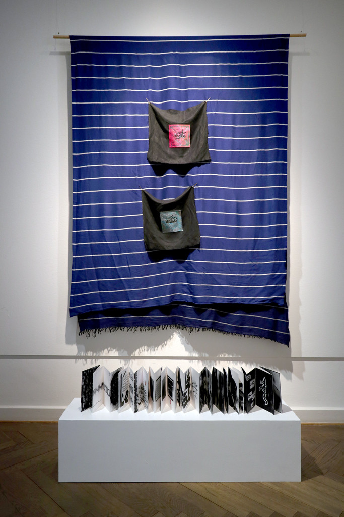 Textil mit zwei arabischen Schriftzeichen mit ausgebreitetem Buch davor