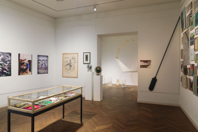 Innenansicht der Galerie im Saalbau. Zu sehen sind eine Vitrine und mehrere an die Wand gehängte Kunstwerke so wie der Durchblick in einen dahinter liegenden Galerieraum.